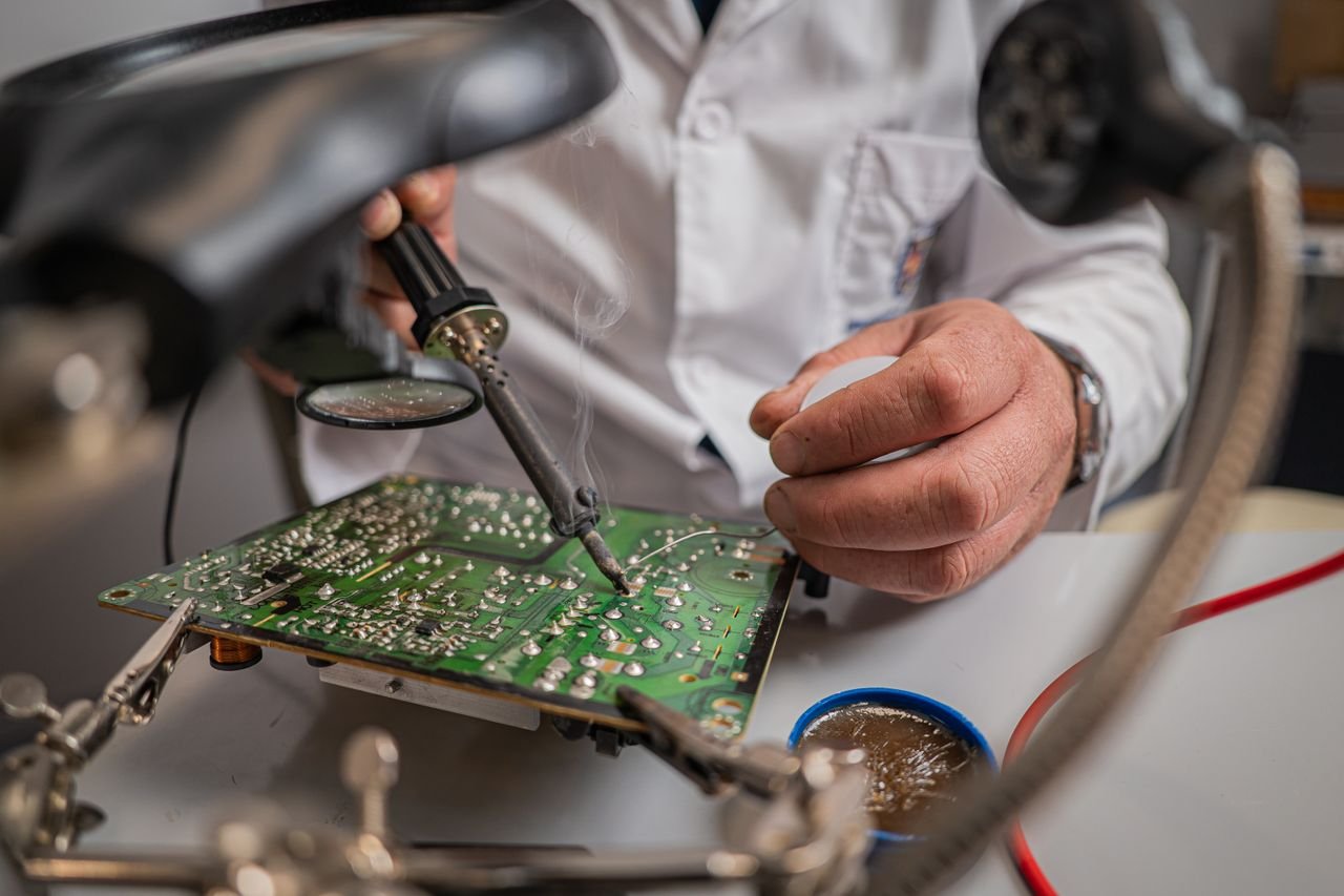 Close-up of technician using soldering iron on a circuit board in a lab setting.